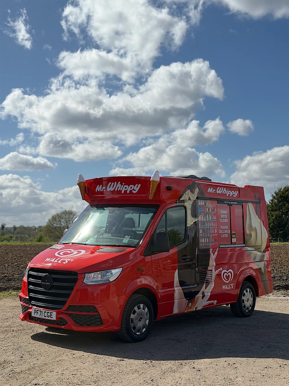 A Kreamy Delights ice cream van in red Mr. Whippy livery under a blue sky, seen from the front corner